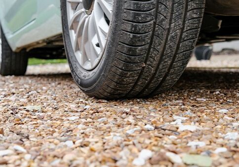 Ground level view of a new car, showing the rear tyre and tread together with the alloy wheel a car parked on a gravel driveway