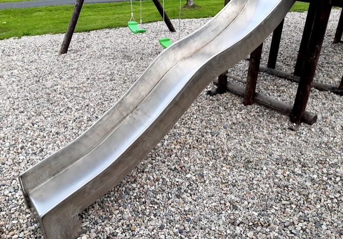 stainless steel slide and swings on the playground in the park in gray pebbles stainless steel slide and swings on the playground that has gravel on the ground